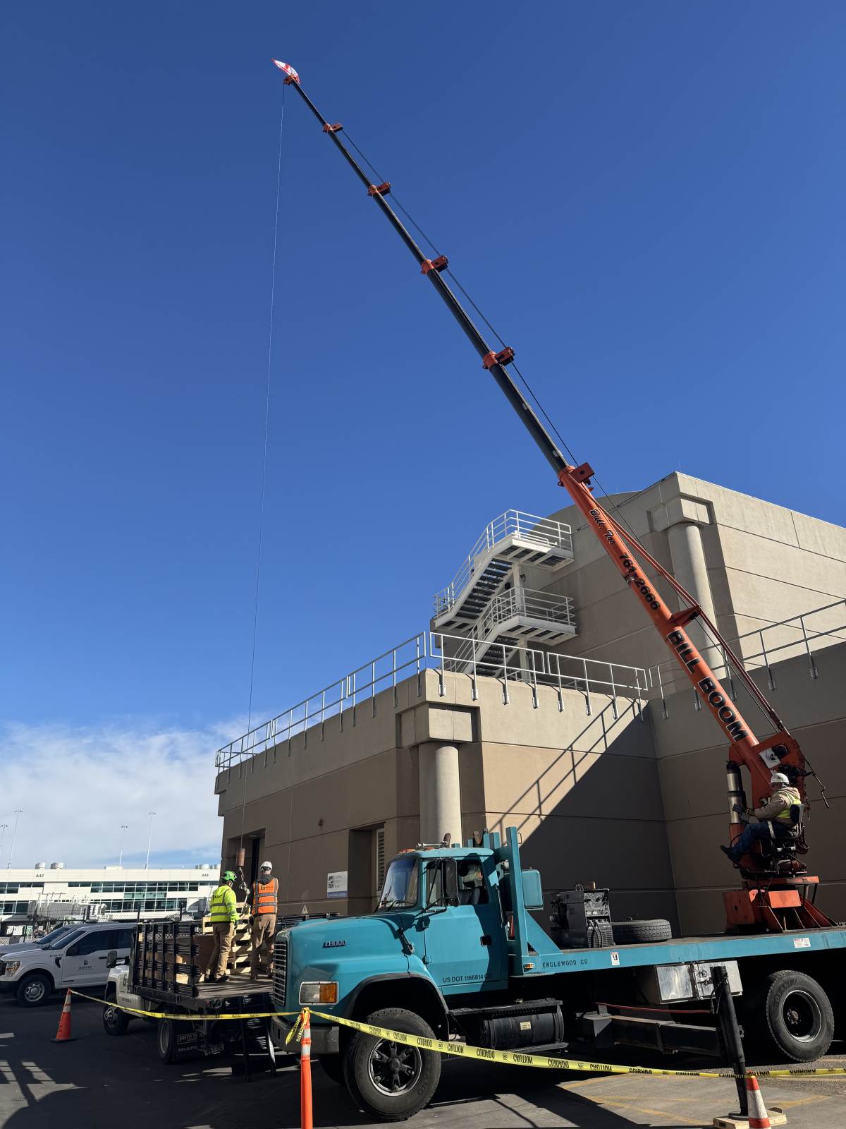 Bill Boom boom truck with boom fully extended lifting at a Denver International Airport utility building