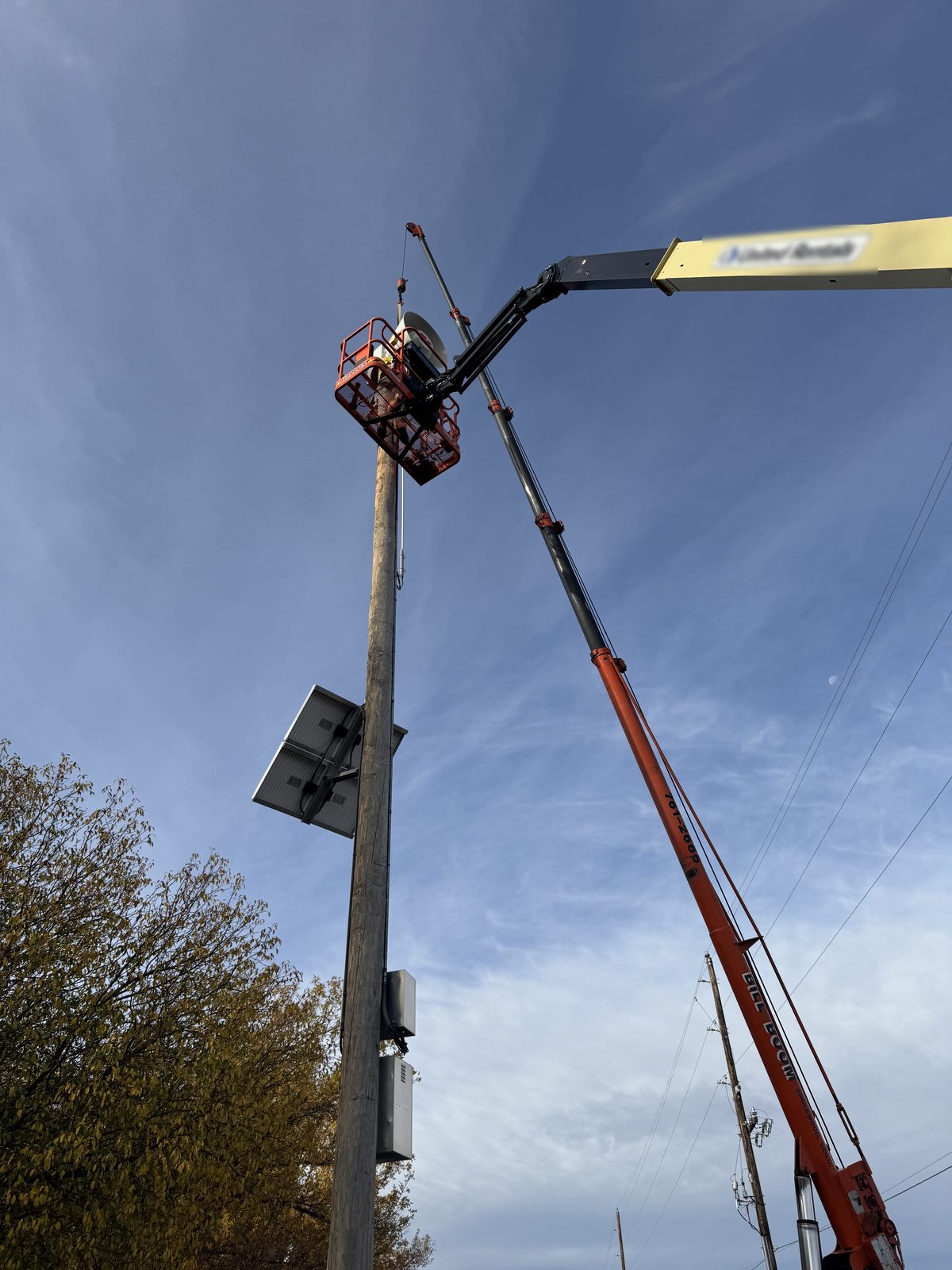 Close-up of a Bill Boom crane hook and a boom lift basket at the top of a siren pole with power lines nearby