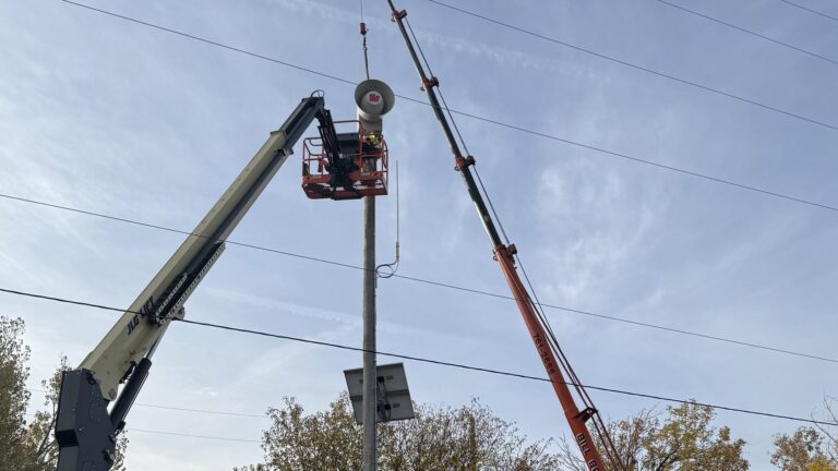 Bill Boom boom truck crane lifting a tornado warning siren head onto a 50-foot pole on a residential street in Aurora, Colorado