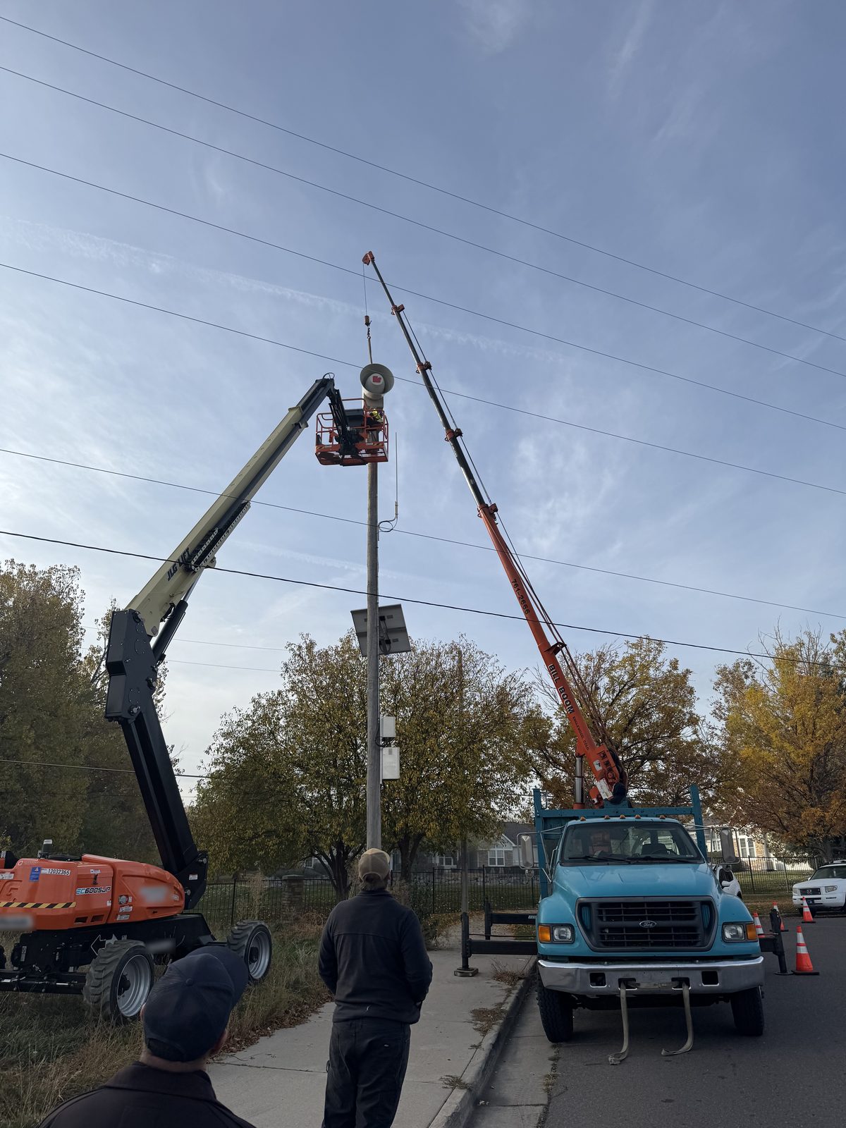 Bill Boom boom truck crane lifting a tornado warning siren head onto a 50-foot pole on a residential street in Aurora, Colorado